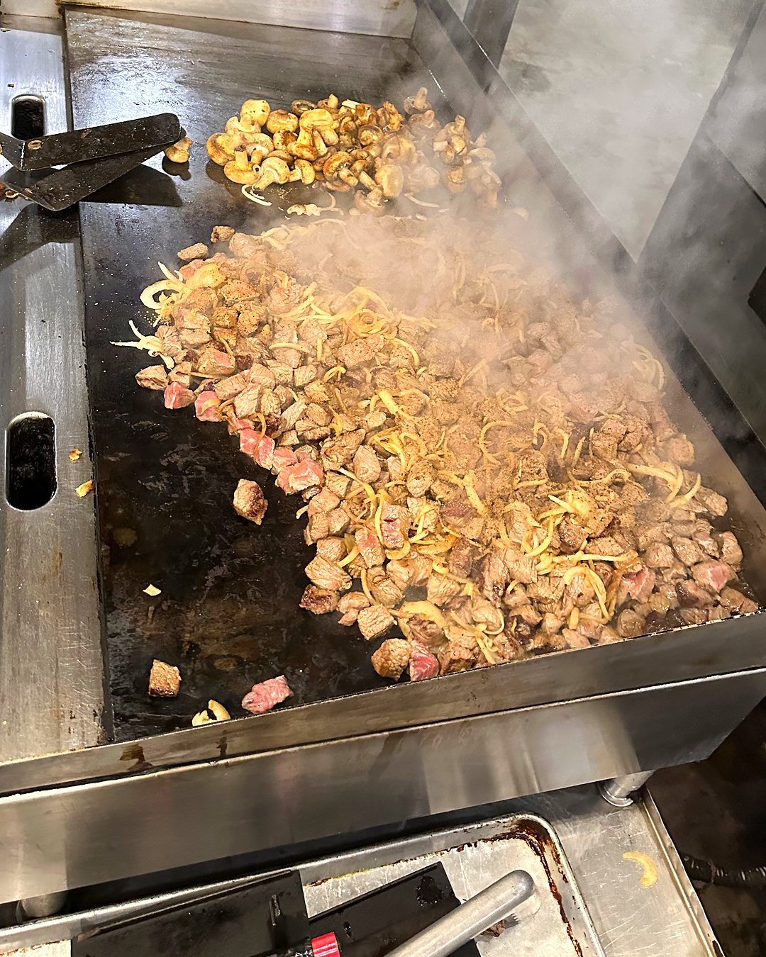 Meat, onions and mushrooms sizzling on the flat-top grill